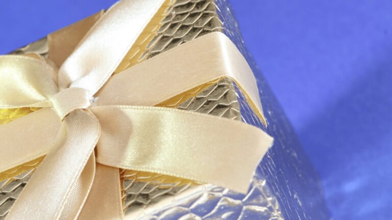 Pile cadeau ornementée d’un ruban satin crème, entourée de filet doré, sur fond bleu, parfait pour une occasion spéciale.