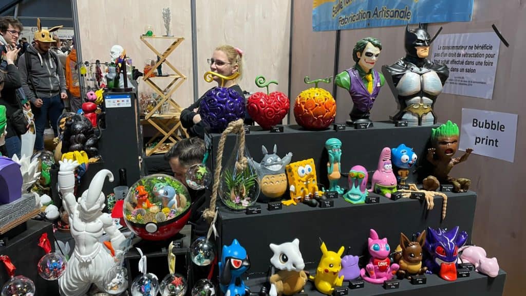 Poupées artisanales en résine et art numérique Bubble print exposées lors de la foire d'artisanat et de collection. Figurines originales inspirées de pop culture dans un stand coloré et créatif.