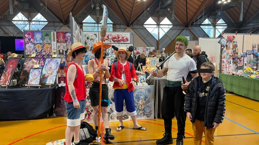 Cosplayers déguisés en personnages d'anime avec des tatouages, exposant des œuvres d'art lors d'un salon de manga et de jeux vidéo.