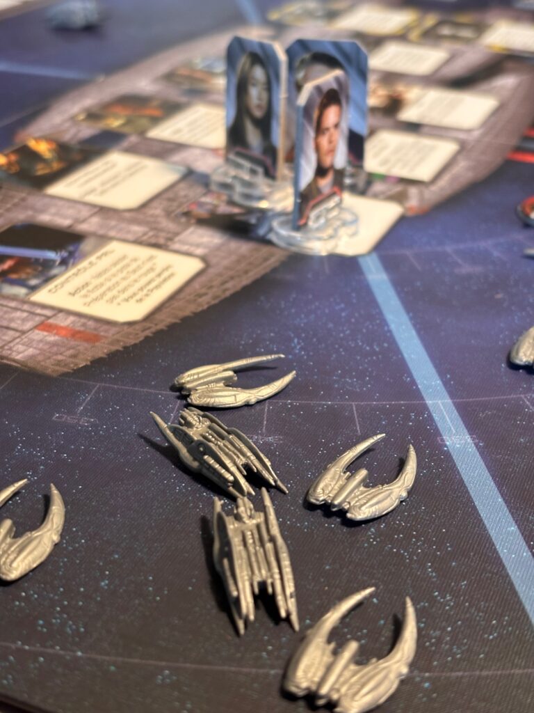 Flèches en plastique argenté du jeu de société Star Wars: Outer Rim avec cartes et figurines de personnages futuristes sur un tapis de jeu spatial.