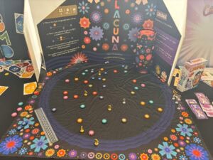 Lancez une partie de jeu de société autour de "La Cuna" sur le stand air-gaming, avec des plateaux colorés, des pièces de jeu et des règles pour une expérience ludique et immersive.