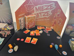 MIEZE KATZE, jeu de société sur le thème félin, avec composants colorés, jetons et figurines d'animaux, présenté sur un stand d'exposition.