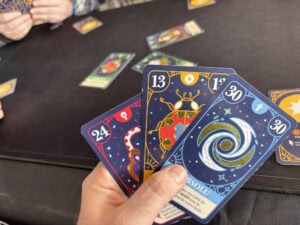 Cartes de jeu de société colorées avec motifs artistiques et numéros, utilisées pour jouer à un jeu stratégique ou de cartes dans un environnement convivial et compétitif.