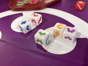 Lancement des dés colorés lors d'une partie de jeux de société, avec un fond violet et une mise en scène ludique pour des sessions de gaming amusantes.