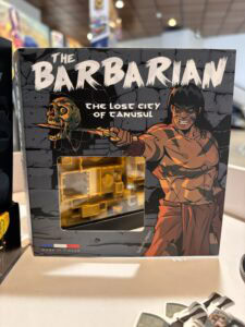 Étiquette alt : Boîte de jeu de société "The Barbarians: The Lost City of Tanusul" avec illustration d'un guerrier barbare et un crâne.