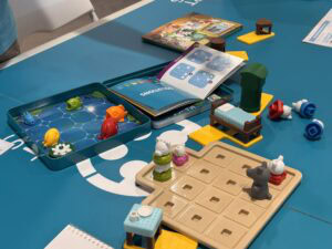 Petits jeux de société et jouets en plastique colorés sur une table bleue, incluant des figurines d'animaux, un livre de règles, et un plateau de jeu, parfaits pour enfants et activités familiales.