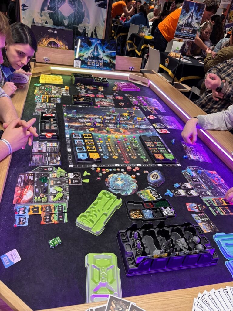 Fichiers de jeu de société sur un stand de gaming, avec des figurines, cartes et jetons, lors d'une convention de jeux vidéo et de société.