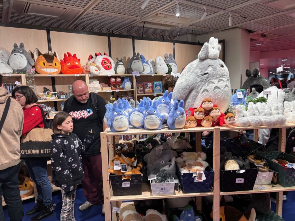 Peluches de personnages de film Totoro sur un stand d’exposition, ambiance de salon de gaming ou cosplay avec décoration de geek, jouets et produits dérivés.