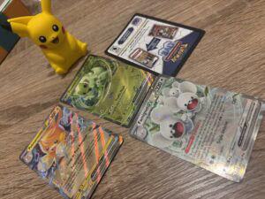 Pikachu en plastique jaune à côté de cartes Pokémon brillantes et héros Pokémon sur une surface en bois.