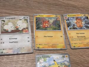 Cartes Pokémon illustrées avec Pokémon type feu et normal, incluant Pikachu, Pohm et Pohmotte, disposées sur une surface en bois.