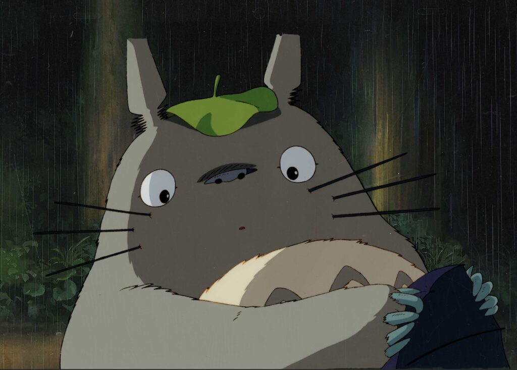 Un personnage de film d'animation Totoro, dans un décor de forêt sous la pluie, avec un chapeau vert, illustrant l'univers du jeu vidéo Air-Gaming.