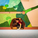 TEXTE ALT: Enfant souriant dans une pièce d'arcade ou salle d'activités avec un mur mural coloré représentant un paysage de nature.