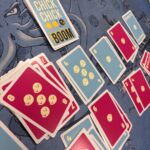 Poules et dés en jeu de cartes Chick Chick Boom sur un tapis de jeu bleu avec illustrations.