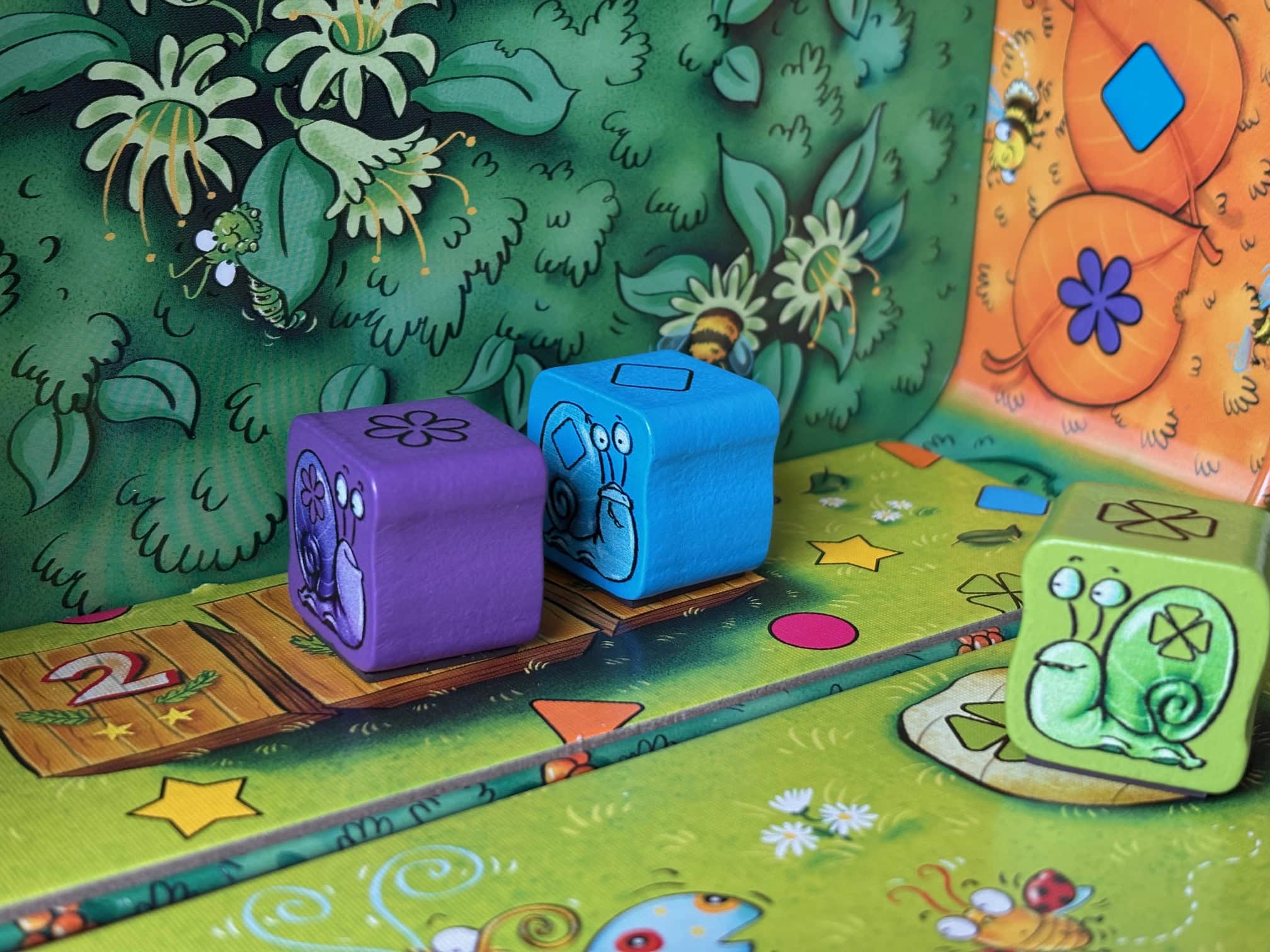 IMG_7959 Colorful game pieces with snail illustrations on a vibrant, animated board game scene for children, featuring playful, cartoon-style art and bright colors.