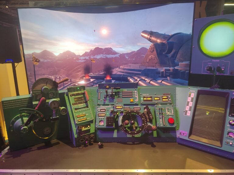 Simulateur de avion militaire avec tableau de bord détaillé et jeu de simulation de vol avec vue sur montagnes enneigées et canon futuriste en arrière-plan.