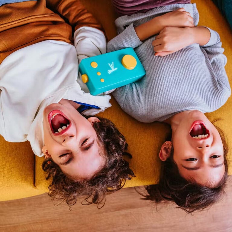 Joueurs d'enfants riant sur un canapé avec une manette de jeu vidéo colorée, jeux vidéo pour enfants, console de jeux, divertissement familial, activités ludiques pour enfants.