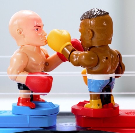 Des poupées boxeurs en position de combat sur un ring, symbolisant la compétition et l'esprit sportif, avec des détails contrastés et une mise en scène dynamique.