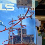 Tuyau de train à billes Sky Trails pour enfants, en édition Playmobil, structure colorée et ludique sur un fond ciel bleu, idéale pour jeux et activités en famille, salon de jouets ou événement ludique.