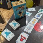 Un jeu de société "Le Baron" avec des cartes illustrées de figures de dragons et de monstres, sur une table en bois, utilisé pour des activités ludiques et sociales lors d'une session de jeu.