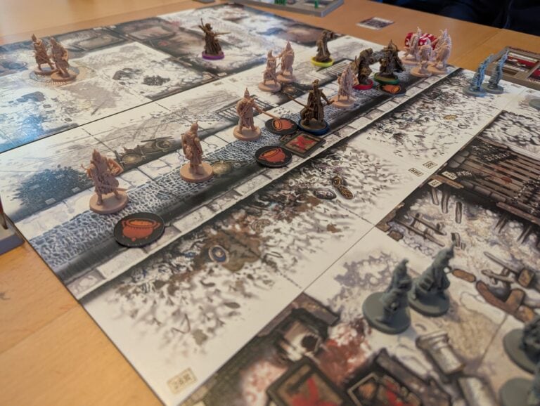Des figurines et plateaux de jeu pour une partie de jeu de société d'horreur et de stratégie, inspirée de l'univers de horror et de fantasy, avec des éléments de décor enneigé et chaos.