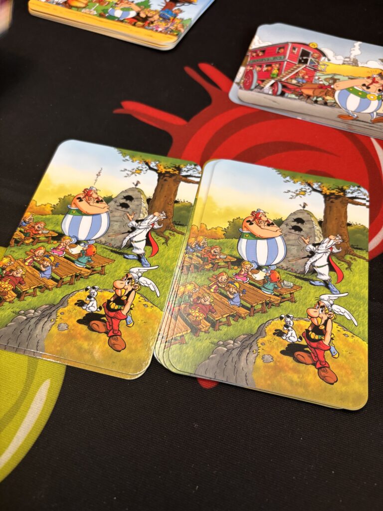 Des cartes de jeu de société avec des illustrations de dessins animés de la bande dessinée Astérix et Obélix, mettant en scène des personnages célèbres dans un décor coloré et ludique.