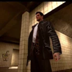 Un homme debout dans un métro ou un tunnel, portant un manteau en cuir noir et un foulard léopard, dans un environnement urbain sombre avec des murs en céramique beige.