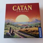 Jeu de société Catan avec paysage rural, montagne et mer au coucher du soleil, idéal pour les amateurs de divertissement convivial et stratégique.