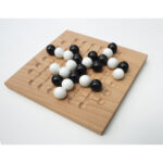 Jeu de morpion traditionnel avec pions noirs et blancs sur plateau en bois naturel, idéal pour jeux de société et divertissement familial.