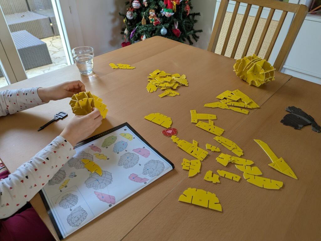 Puzzle de construction pour enfants, activité ludique avec pièces jaunes, manuel d'instructions visible, ambiance festive avec sapin de Noël décoré, idéal pour sensori-moteur et créativité.
