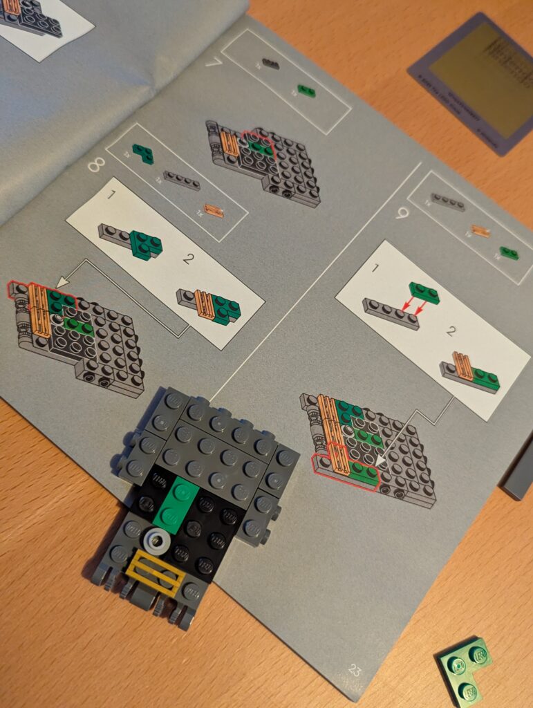 Description d'image : Planche d'instructions LEGO avec pièces en cours de construction, notamment un véhicule ou un personnage, accompagné d'une pièce déjà assemblée.