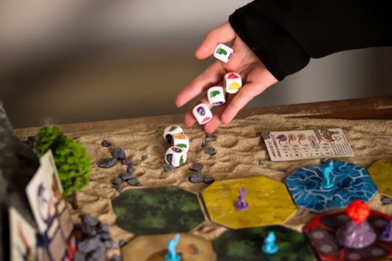 ALT: Personne manipulant des dés colorés lors d'une partie de jeu de société, entourée de tuiles, cartes et figurines, idéal pour les amateurs de jeux de stratégie et de divertissement en famille ou entre amis.