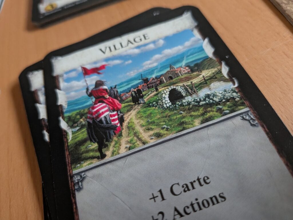 Village médiéval illustré sur une carte de jeu, représentant un paysage de campagne avec un chevalier en armure, un village historique, pont en pierre, et paysages bucoliques, idéal pour jeux de société ou collection.