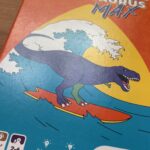 Jeu de cartes familial avec un dinosaure surfant sur une vague, idéal pour jouer en famille et développer la stratégie.