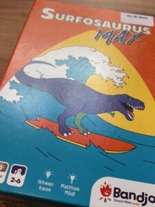 Jeu de cartes familial avec un dinosaure surfant sur une vague, idéal pour jouer en famille et développer la stratégie.