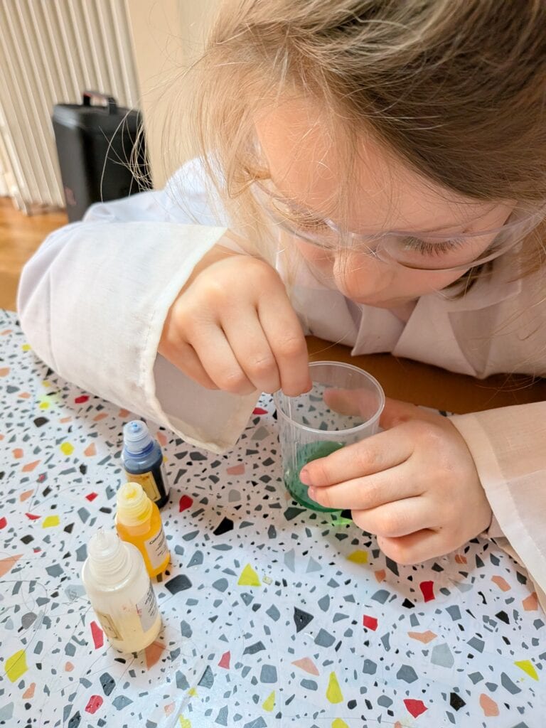 Enfant réalisant une expérience scientifique avec des liquides colorés dans un verre, illustrant la curiosité et l'apprentissage ludique.