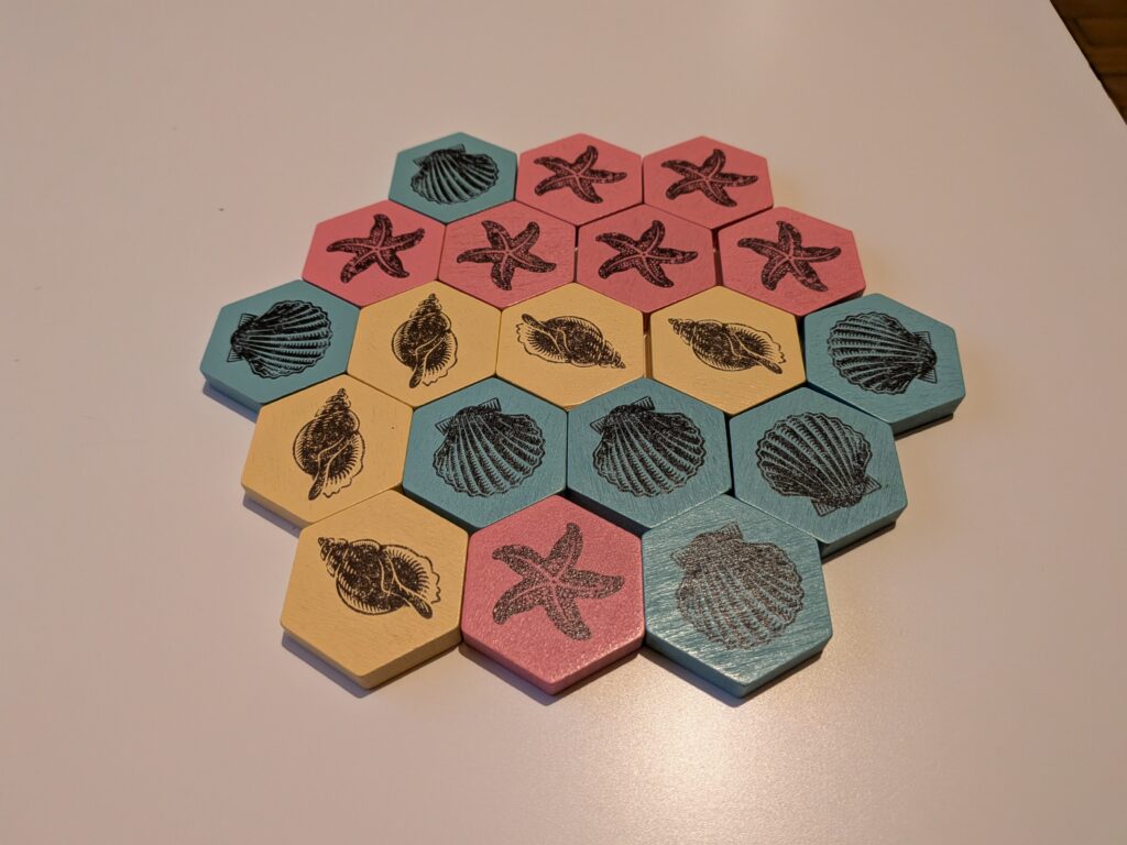 Jeu de société avec tuiles hexagonales illustrant des coquillages et étoiles de mer, évoquant la marée haute et l'océan. Parfait pour les amateurs de jeux de stratégie et de thèmes marins.