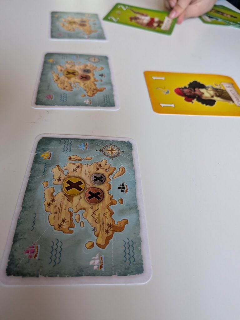 Jeu de société "Hisse et Oh" avec cartes et cartes illustrées représentant des îles et des pirates, parfait pour les amateurs de jeux de stratégie et d'aventure maritime.