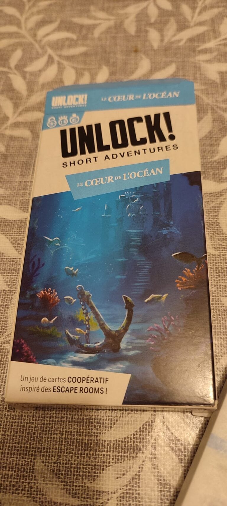 Jeu de cartes coopératif inspiré des escape rooms, illustrant un univers sous-marin mystérieux avec des coraux, poissons et ruines englouties, parfait pour une aventure immersive.