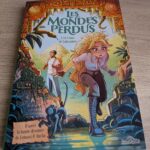 Une couverture de bande dessinée illustrée représentant une jeune fille avec des cheveux longs et bouclés, explorant une jungle mystérieuse avec un crâne ancien et des statues en pierre, évoquant l'av.