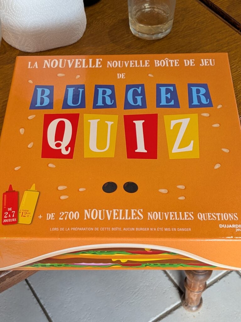 Jeu de société Burger Quiz avec boîte colorée, contenant 2700 questions pour tester vos connaissances et votre esprit d'équipe, idéal pour soirées entre amis ou en famille.