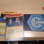 Jeu de société avec cartes illustrées représentant des stratégies de trahison et de combat, sur une table en bois avec jetons rouges.