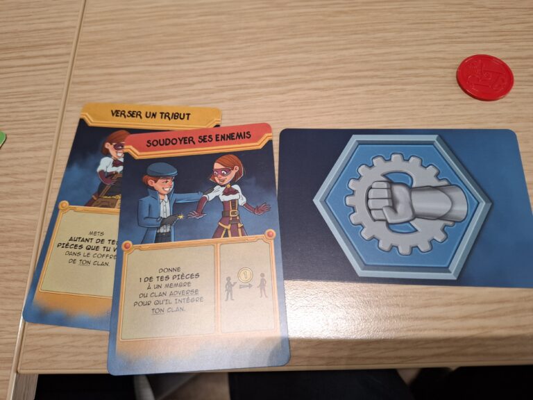 Jeu de société avec cartes illustrées représentant des stratégies de trahison et de combat, sur une table en bois avec jetons rouges.