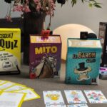 Jeux de société et cartes pour enfants et adultes sur une table, incluant quiz, personnages de manga et jeux de stratégie.