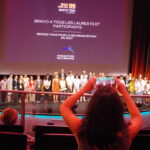 Groupe de lauréats et participants lors de la cérémonie de remise des prix Space Game Jam 99 en 2027, sur scène avec écran de fond.