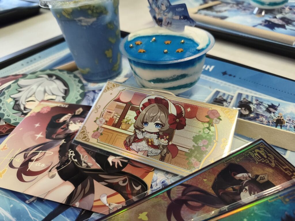 Objets liés à Genshin Impact, incluant des figurines, cartes et accessoires, présentés sur une table avec des boissons et des jeux.