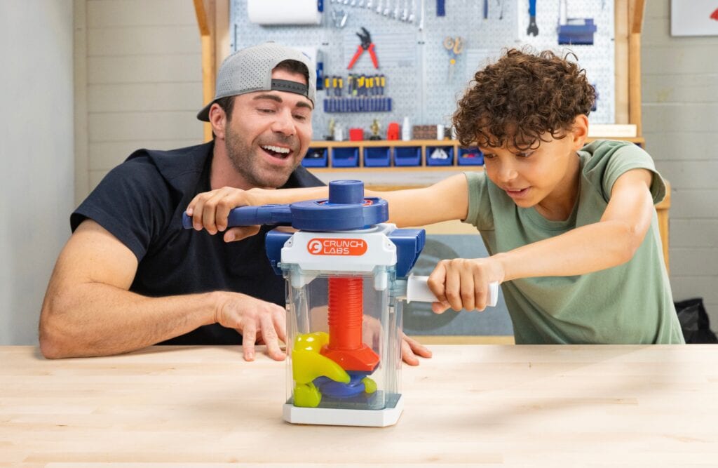Un adulte et un enfant jouent avec un jeu de science CrunchLabs, explorant la physique et l'ingénierie ensemble.