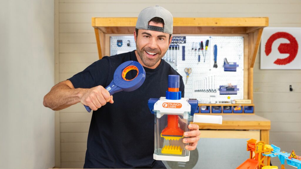 Homme souriant utilisant un jeu scientifique éducatif avec un marteau et un mécanisme de science pour enfants dans un atelier.