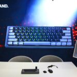 Clavier gaming ultra-large avec rétroéclairage RGB présenté lors de la Gamescom 2026, avec accessoires et écran interactif à côté.