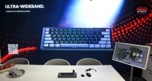 Clavier gaming ultra-large avec rétroéclairage RGB présenté lors de la Gamescom 2026, avec accessoires et écran interactif à côté.
