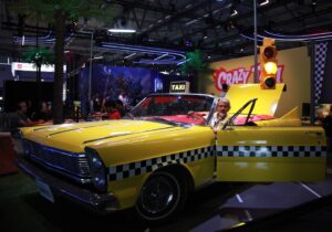 Taxi jaune de Crazy Taxi exposé à Gamescom 2026 avec décor coloré et ambiance animée.
